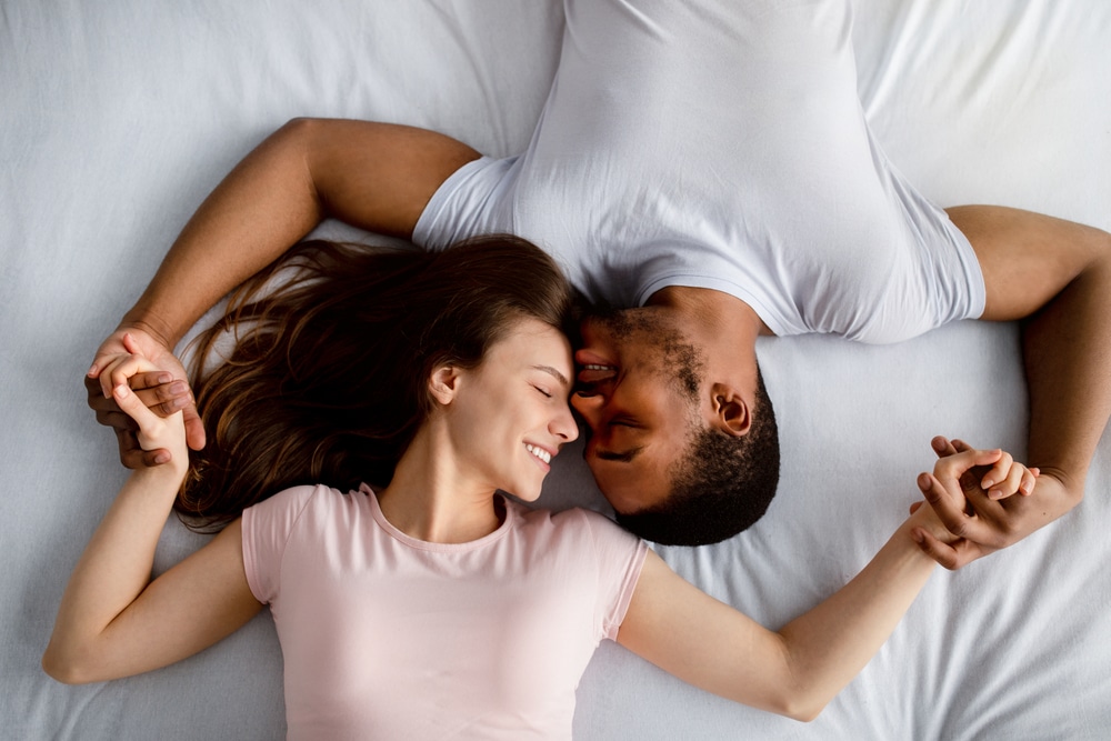 Top,View,Of,Young,Multiracial,Couple,Lying,On,Bed,,Cuddling,
