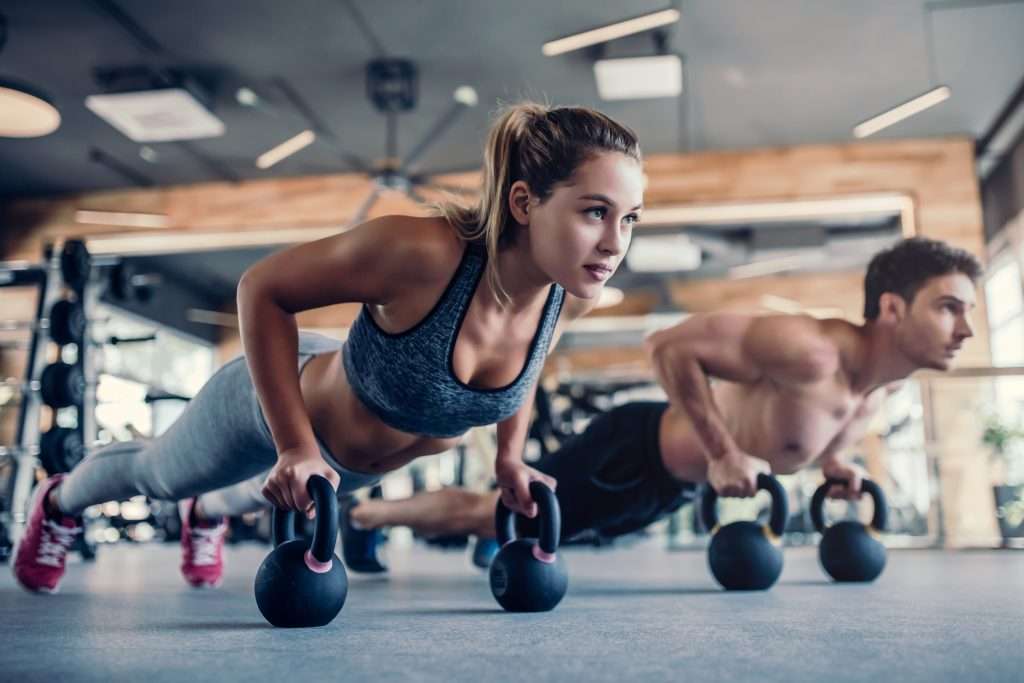 Couple in gym doing kettlebell pushups