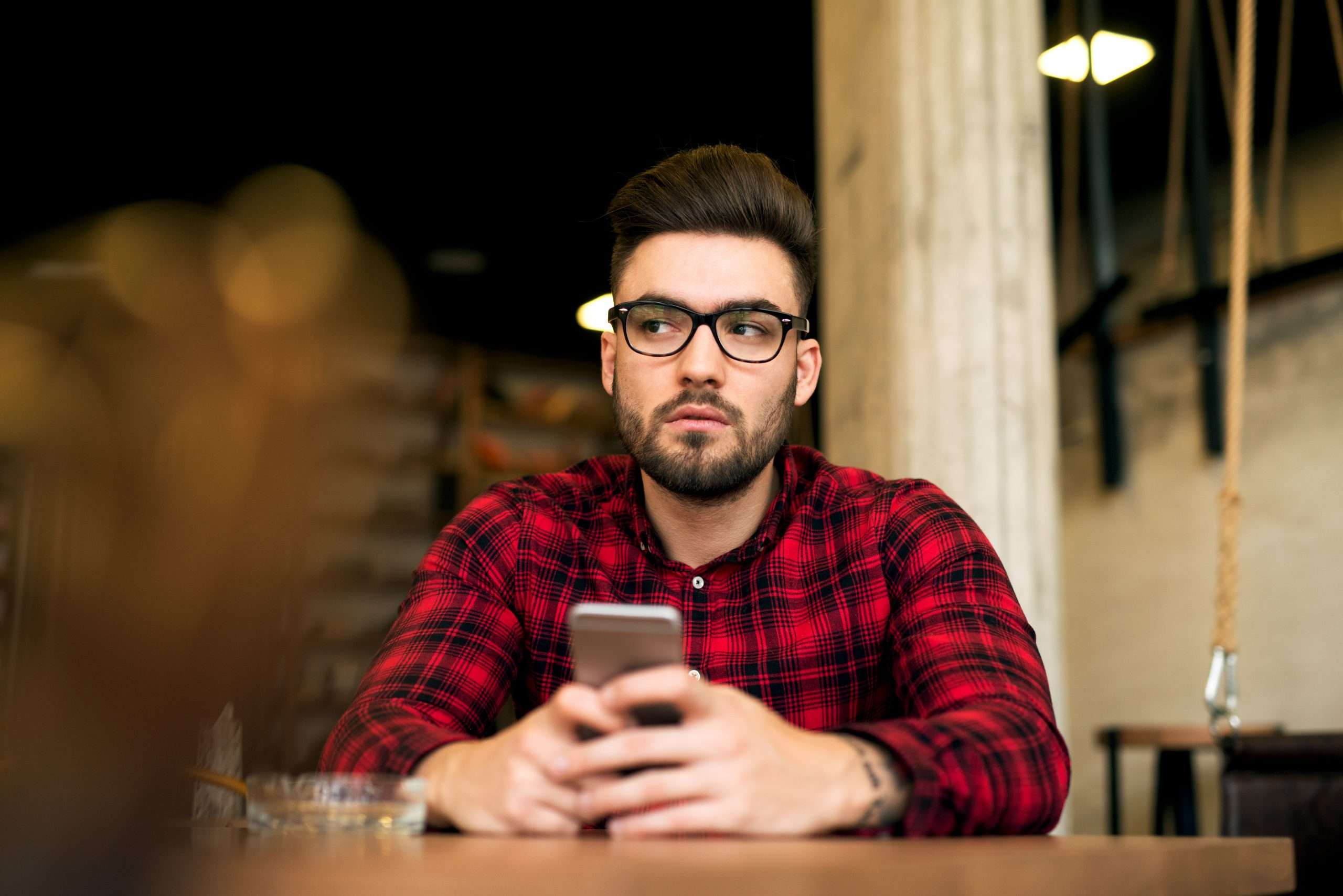 Young handsome hipster guy with beard and glasses sitting in a c