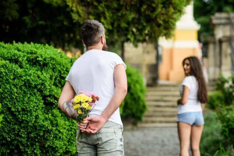 Man Looking at Woman with Flowers Behind his Back