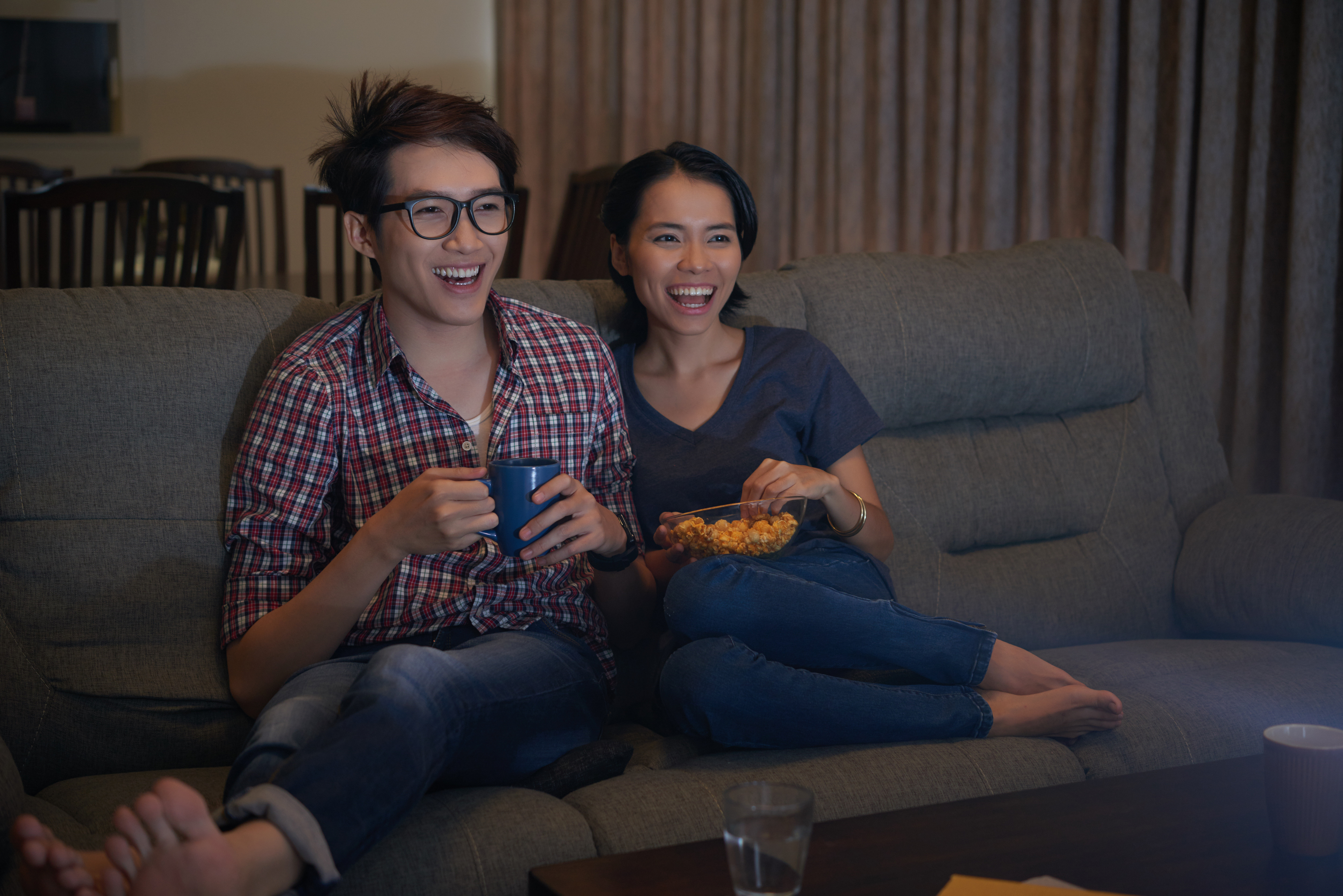 Young Asian couple laughing at a TV program