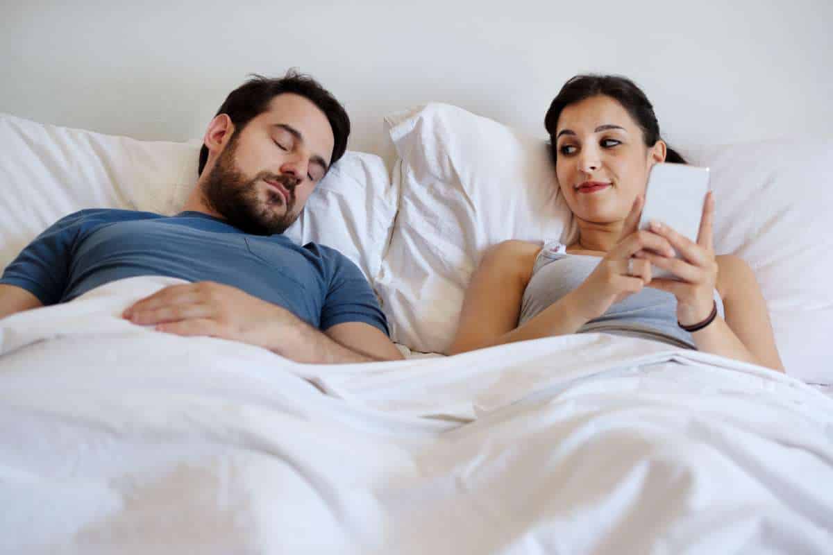 Woman texts on phone while man is sleeping