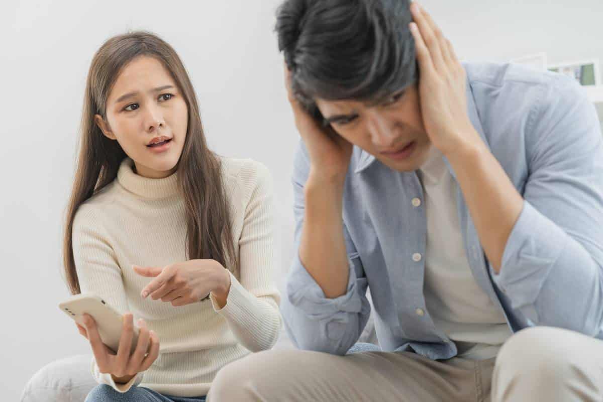 Young Asian couple, woman questioning man about contents of phone