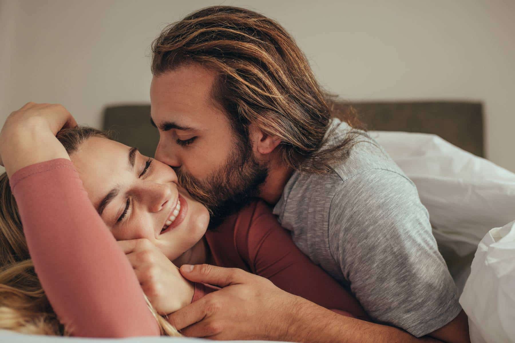 couple in bed, man kissing woman on the cheek and she's smiling